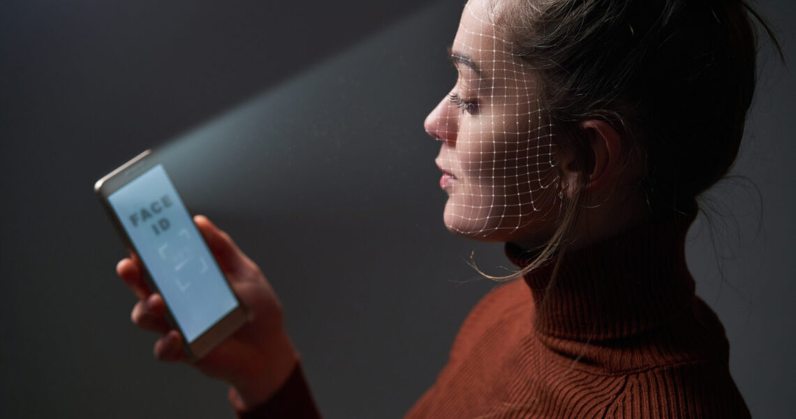 Female scans face using facial recognition system on mobile phone for biometric identification. Future hi tech technology and face id
